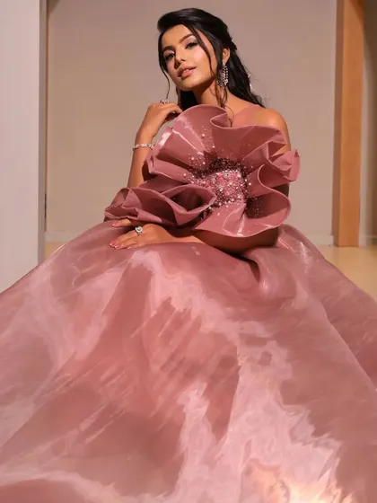 A full shot of the model in a dramatic pink gown. The soft, romantic hairstyle provides a gentle contrast to the large structural flower on the dress.