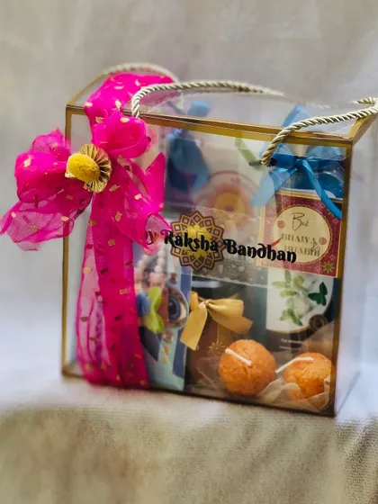 A vibrant Rakhi gift bag with a bright pink bow, filled with sweets and self-care items.