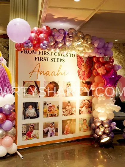 A first-year milestone photo board for a princess party, featuring a Rapunzel cutout and a balloon arch in shades of pink, purple, and silver.