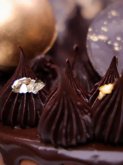 We indulge the senses with this elegant chocolate drip cake. A rich chocolate cake is topped with a fan of decorative chocolate, gold spheres, and delicate gold leaf accents, making it a sophisticated and decadent choice for Father's Day.
