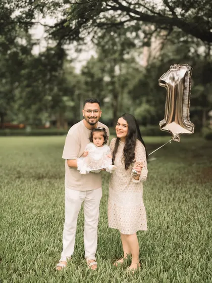 A classic family portrait in the park, celebrating a first birthday with a special balloon.