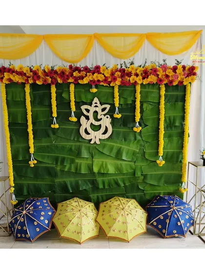 A classic backdrop for a naming ceremony or puja, using a wall of banana leaves, marigold garlands, and a wooden Ganesha cutout.