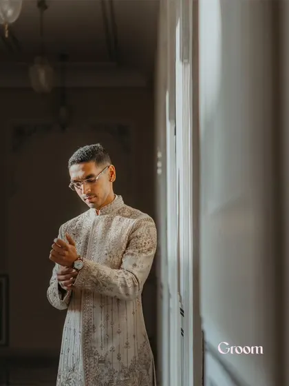 A candid portrait of the groom adjusting his cufflink, captured in soft, natural light.