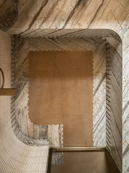 An overhead shot of the shower area, showing the intricate detail of the fluted marble skirting that meets the micro-concrete floor.