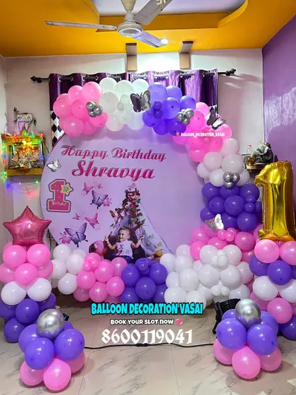 Shravya's butterfly-themed first birthday. This home setup features a round photo backdrop and a balloon arrangement in purple, pink, and white.