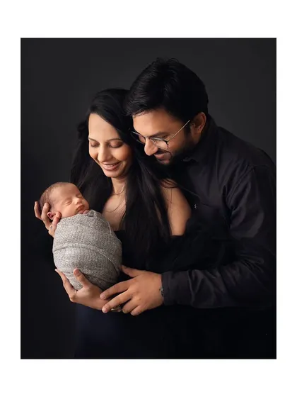 A classic family portrait against a dark backdrop, with both parents holding their new baby.