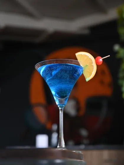A vibrant blue cocktail in a martini glass, garnished with an orange slice and a cherry. It's a drink that's guaranteed to brighten up your night.