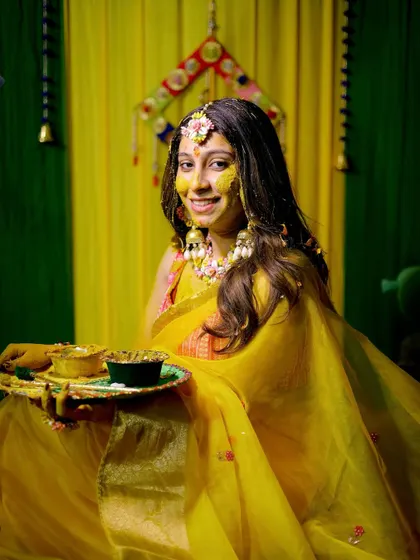 The bride, glowing in yellow, holds a thali during her Haldi ceremony, ready for the rituals to begin.
