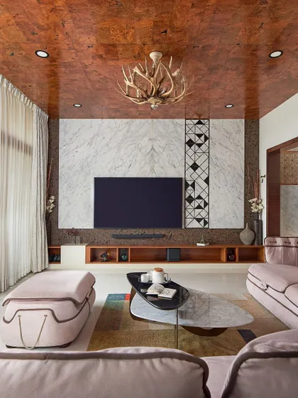 For the Sobha Indraprastha residence, we designed a living room that exudes opulence. The combination of a rich, wood-veneered ceiling, a book-matched marble accent wall, and a unique antler chandelier creates a luxurious and detail-oriented space.