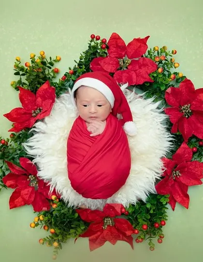 A full view of the Christmas wreath setup. The baby is swaddled in red and nestled in a fluffy white center, looking like the most precious holiday gift.