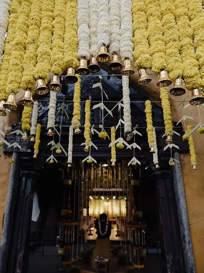 A beautiful decor detail shot of a floral archway made of yellow and white flowers, adorned with traditional temple bells. This image captures the festive and sacred atmosphere.
