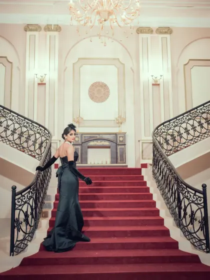 A glamorous pre-wedding shot of a woman in a black gown on a grand red staircase, evoking a sense of drama and elegance.