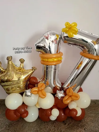 A custom 17th birthday balloon bouquet with silver numbers, a gold crown, and a base of brown and cream-colored balloons.