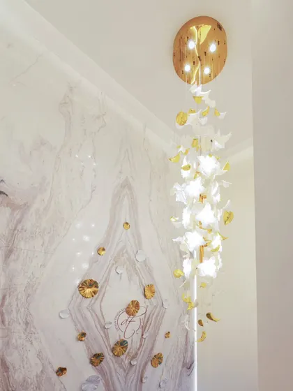 A close-up of the cascading chandelier, which is made of custom white and gold elements. It hangs through the double-height space, illuminating the staircase and the feature wall.