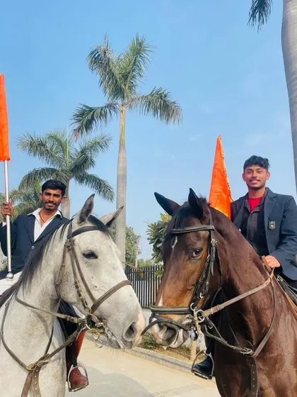 Two of our riders on horseback, holding flags, during a ceremonial event. They represent the pride and spirit of our academy.