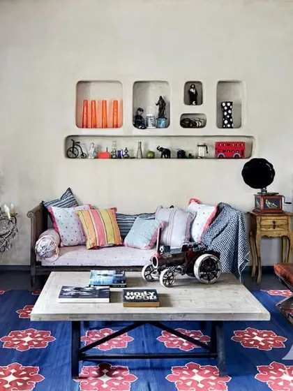 An eclectic living room we designed for Kangana Ranaut, featured in Architectural Digest. The space is a vibrant mix of colors, textures, and personal objects, including a bold blue rug and a gallery wall of memories.