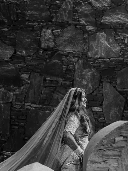 A timeless black and white portrait of the bride. The stone wall background provides a beautiful texture, and her joyful expression is captured perfectly as she looks away from the camera.