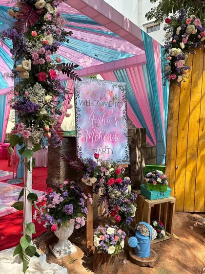 A personalized welcome sign at the entrance, surrounded by lush floral arrangements, set the perfect tone for this colorful Mehendi party.