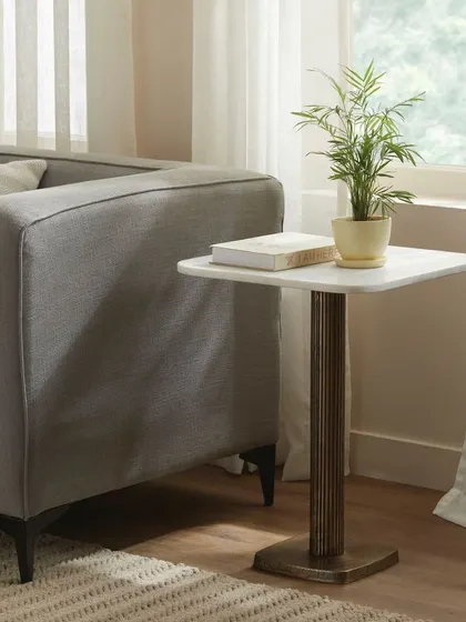A square marble-topped side table, positioned next to a sofa. The image showcases how the piece functions in a living room setting, emphasizing its practicality and style.