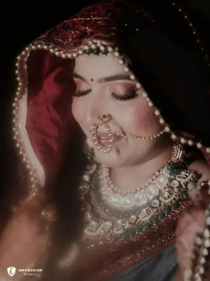 A beautiful close-up of the bride, her face partially covered by her dupatta, smiling shyly. The lighting is warm and romantic.