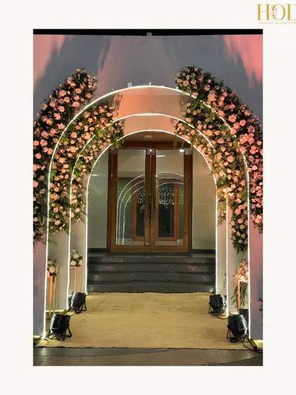 A beautiful floral archway entrance for an evening event. The repeating arches are adorned with soft pink roses and illuminated with gentle backlighting, creating a romantic and dreamy welcome.