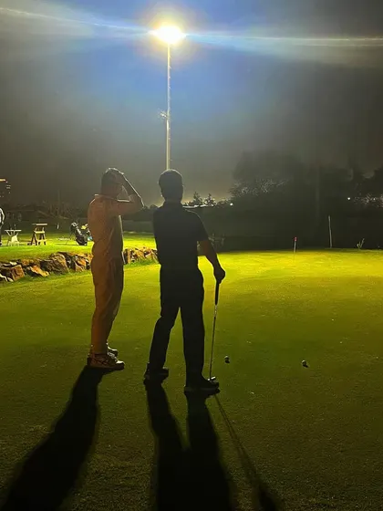 Two players discuss strategy on the putting green under the bright floodlights. The game doesn't stop when it gets dark here.