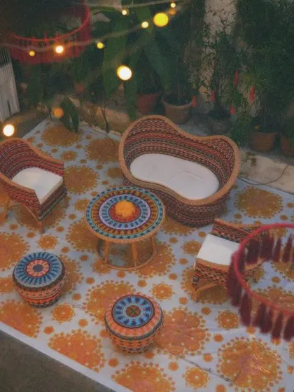 A cozy outdoor seating arrangement for a mehendi night. The patterned rug, cane furniture, and warm lighting create an inviting space for guests to relax and mingle.