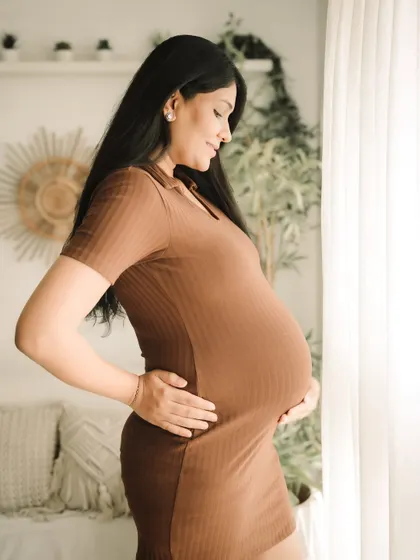 A side profile is a perfect way to document the beautiful curve of your belly. The warm tones of the brown dress and the soft lighting create a gentle and loving portrait.