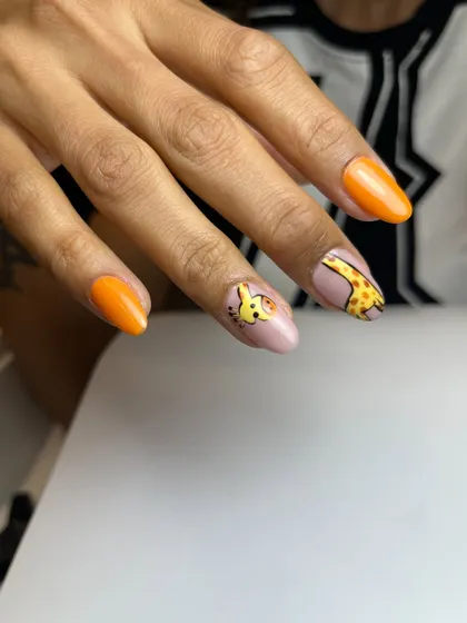 A side view of the cute giraffe nails, showing how the design wraps around the curve of the nail. The bright orange accent nails complete the fun, wild vibe.