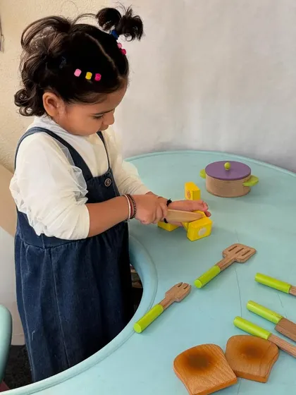 This little chef is busy with a wooden kitchen set. Such imaginative play is crucial for developing life skills, vocabulary, and social-emotional understanding in a fun, hands-on manner.