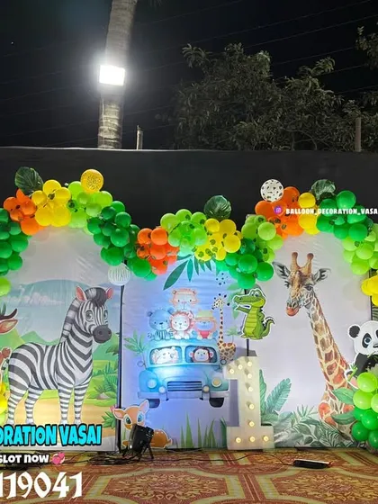 A vibrant animal theme for an outdoor night party. The setup features a large backdrop with various animals and a colorful balloon arch.
