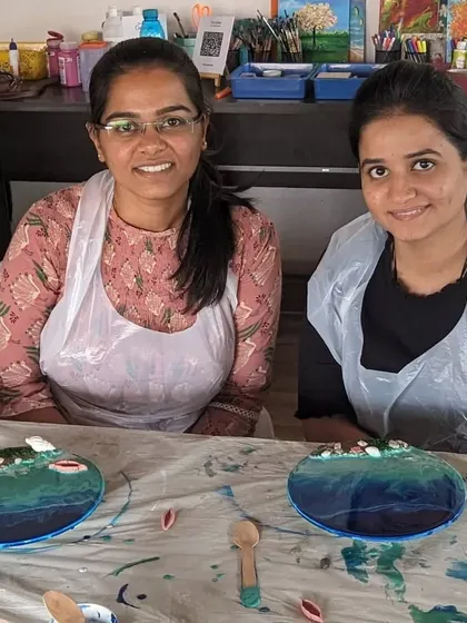 Two friends proudly showing their finished resin beach art pieces. Our workshops are a great way to spend quality time together and leave with a shared memory and a beautiful creation.