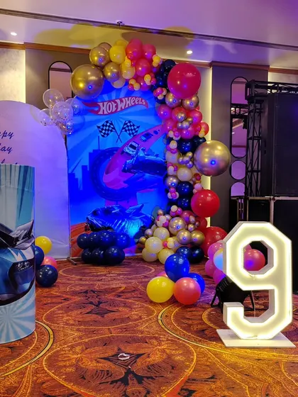 A closer look at the Hot Wheels themed decoration. It includes a custom printed backdrop with race cars, a dynamic balloon garland in red, yellow, and black, and a light-up number '9'.