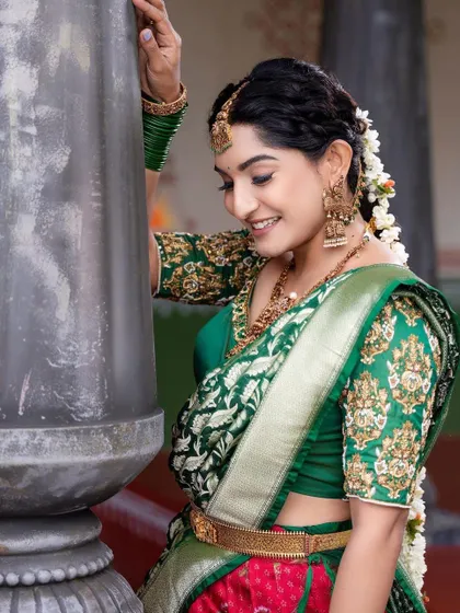 A side view of the client in the green and red half saree, highlighting the embroidered blouse and her braided hairstyle.
