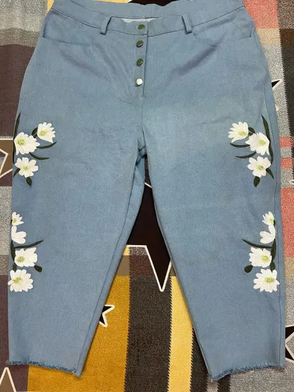 Bring your ideas to life with custom embroidery. These light-wash denim jeans feature a delicate floral design, a button fly, and a modern frayed hem, all tailored to exact measurements.