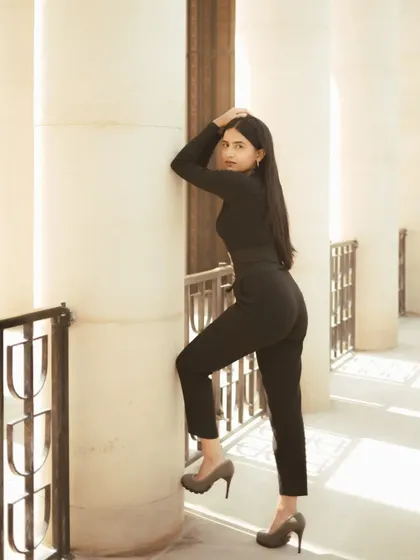 A full-body portrait showing a strong, confident pose against a pillar. The composition uses the repeating lines of the architecture to create a sense of rhythm and elegance.