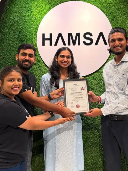 A student proudly holds her TTC certificate, surrounded by her supportive instructors.
