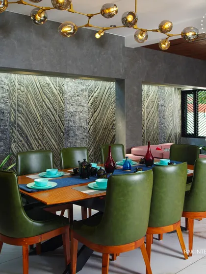 This dining room makes a statement with dark green leather chairs and a textured stone accent wall. The modern branching chandelier provides ample light and acts as a sculptural centerpiece.