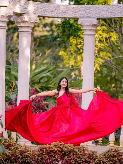 A bright and happy daytime shot at the white pillars. The bride's red gown is spread out, catching the sunlight beautifully and creating a cheerful and elegant portrait.