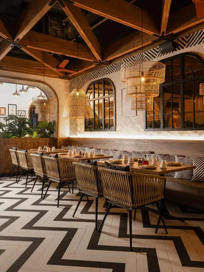 The restaurant's design is a masterclass in pattern and texture, with bold chevron flooring, hand-painted wall motifs, and woven dining chairs.
