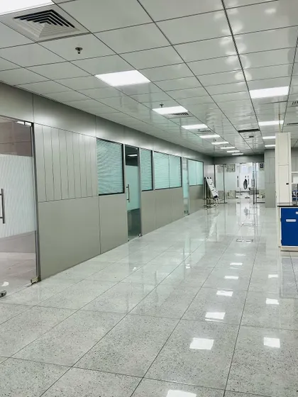 A clean, functional office corridor with polished tile flooring and modular wall panels. Glass doors lead into individual cabins, maintaining a sense of openness while providing acoustic privacy.
