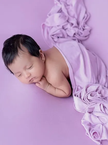 A simple and elegant side-lying pose on a solid lavender background, with the fabric draped artistically.