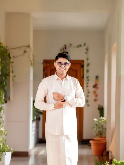 A candid shot of the groom getting ready, adjusting his cuffs in a brightly lit, plant-filled hallway.