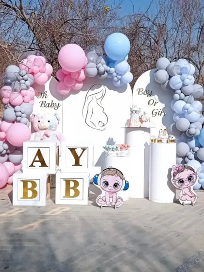 An outdoor 'Boy or Girl' gender reveal party with pink and blue balloon arches, custom backdrops, and 'BABY' blocks.