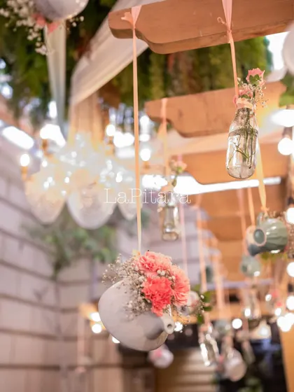 Whimsical hanging decor featuring teapots and teacups used as mini vases for fresh flowers, suspended from a wooden pergola.