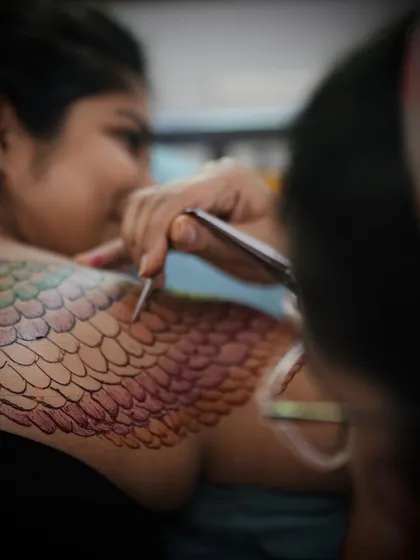 An over the shoulder view of the creative process, showing the colorful henna design taking shape on the model's back.