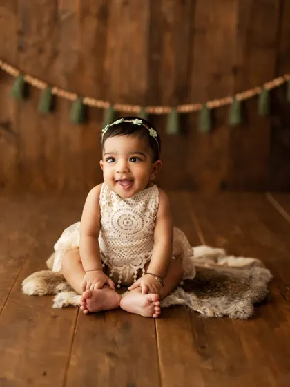 A charming portrait of a baby girl sitting on a fur rug. The simple, rustic setting with a macrame banner is perfect for a sitter session.