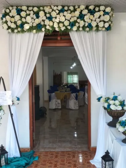 A simple and elegant entrance decoration for a home event, with white drapes and floral arrangements in a blue and white theme.