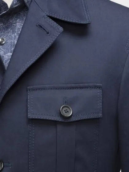A close-up of a navy blue safari-style jacket or waistcoat. The pocket and stitching details show our commitment to quality craftsmanship in every piece.