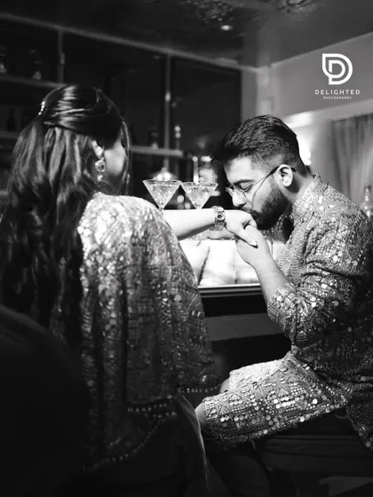 A classic romantic gesture captured in timeless black and white, as the groom kisses the bride's hand during their engagement party.